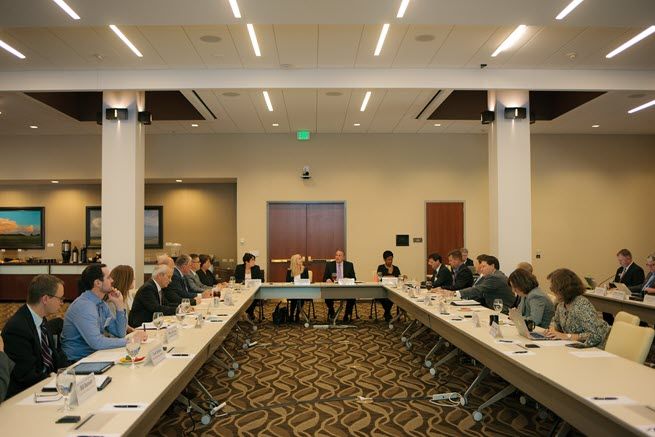 A big room, with three tables arrange in a U shape. Around the table are men and women in business attire.