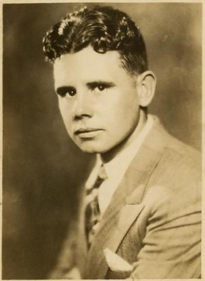 A sepia-toned photo from 1928 of a serious-looking man in his '20s with wavy dark hair, wearing a suit.