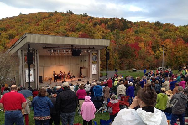 A bluegrass band performs in an outdoor amphitheater on a rainy day in southwest Virginia, watched by hundreds of fans.