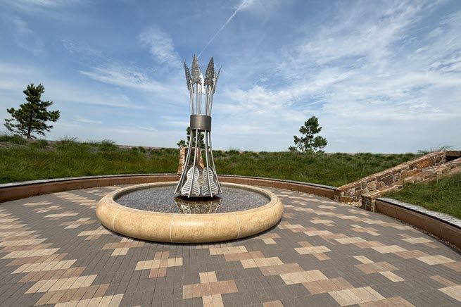 It's a beautiful sunny day in Vinita, Oklahoma. The scene shows a fountain made of huge silver arrows pointing towards the sky, seated in a pool of water, and surrounded by reddish, brown and tan brick.