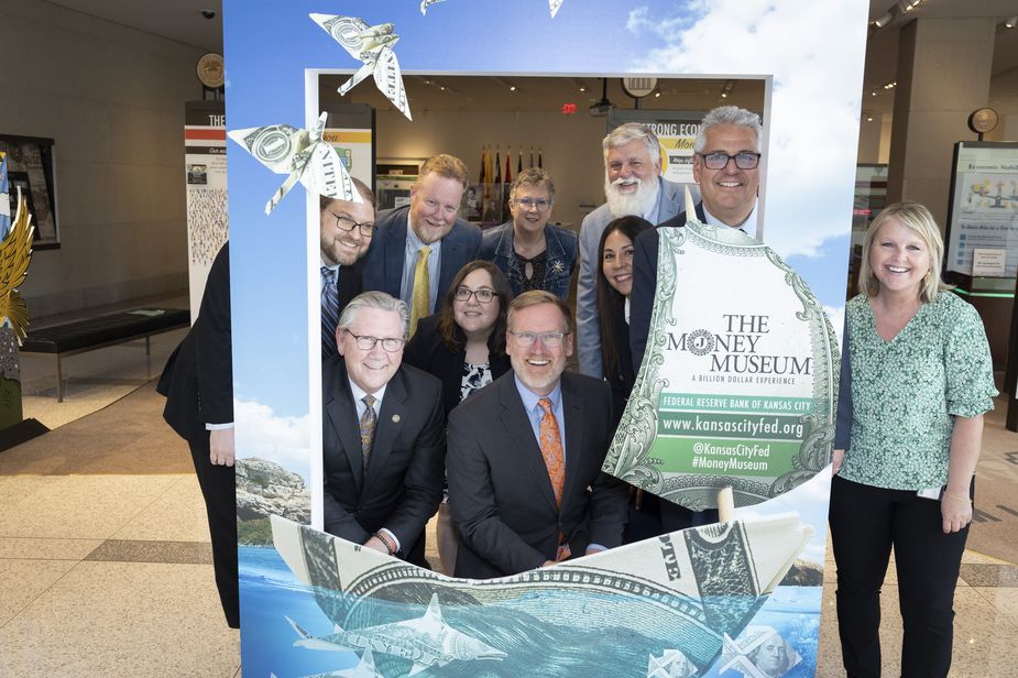 The Money Museum has a big frame where people can post behind the opening for a photo. The group posing today includes ten people, six men and four women. They're smiling, kind of goofy, and appear to be enjoying themselves.