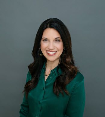 A white woman in her 40s with long brown hair smiles at the camera. She's wearing a green silk blouse.