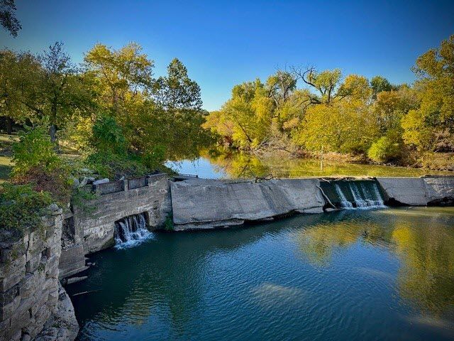 Cottonwoods crowd against a river that flows over a natural stone dam.