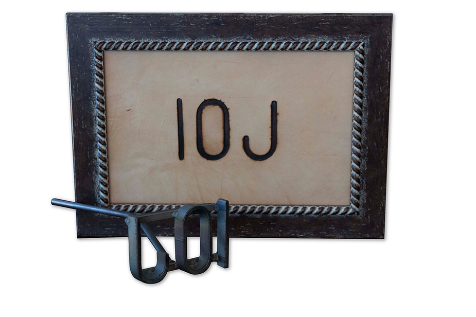 A metal branding iron in the shape of 10J in front of a framed photo showing an example of the brand.