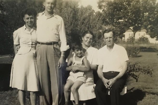 The black-and-white photo, taken in the 1940s or 1950s, shows four adults and one child. Standing, we have Steve's grandma and grandpa, then his dad, a boy of four, is sitting on the lap of his great-grandma, who is seated by her husband.