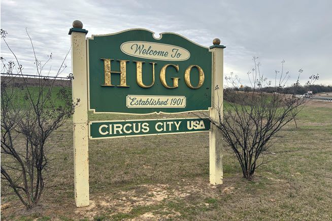 The green-and-white sign, embellished with scrolls, says Welcome to Hugo, Circus City, USA.