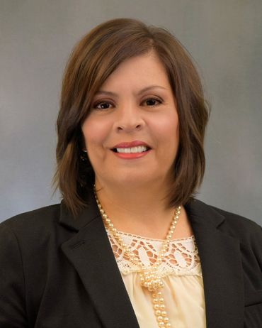Studio head shot of brown-haired woman wearing a black jacket, gold necklace and cream-colored blouse.