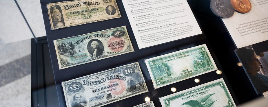 A display case showing various historic U.S. banknotes, each with unique designs and denominations, along with informational placards describing the currency.
