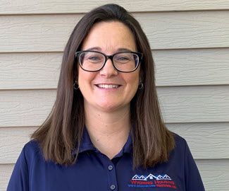 Photo shows a smiling woman in her 30s. She has shoulder-length brown hair and glasses, and she's wearing a blue polo shirt.