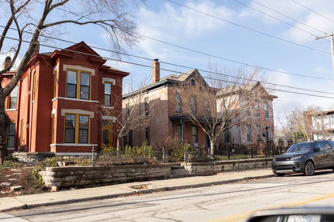 The photo shows three tall brick houses, built in the late 1800s. They sit behind cast-iron fencing that borders the street. They appear to be in great shape.