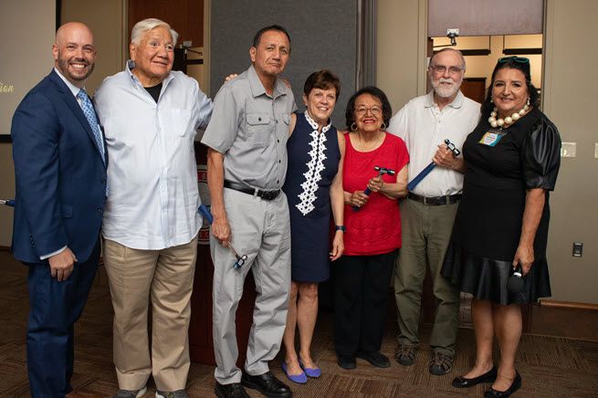 A group photo of five men and three women, some holding hammers, all smiling. Half the group appears to be Hispanic and the others appear to be white. There is a lot of energy and comradeship apparent in the way the people group together.