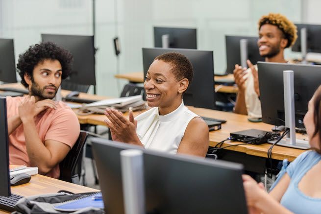 Four college-age students share a laugh as they sit in front of computers in a computer lab.